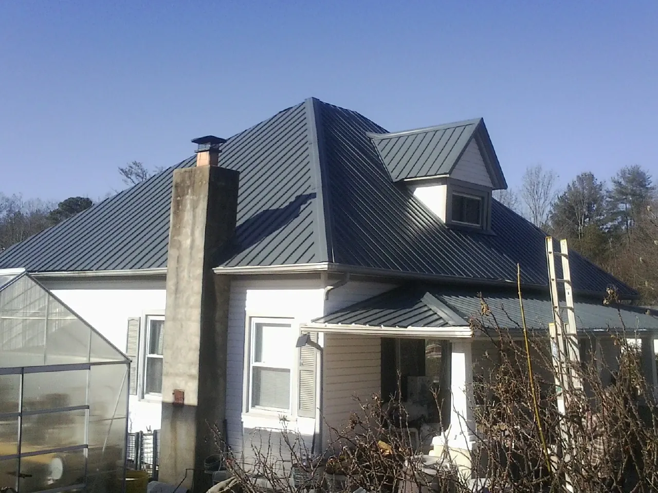 Dark blue standing seam metal roof on a white farmhouse with dormer — Slate & Tile Roof Repair by Roofing Brothers in Olsburg
