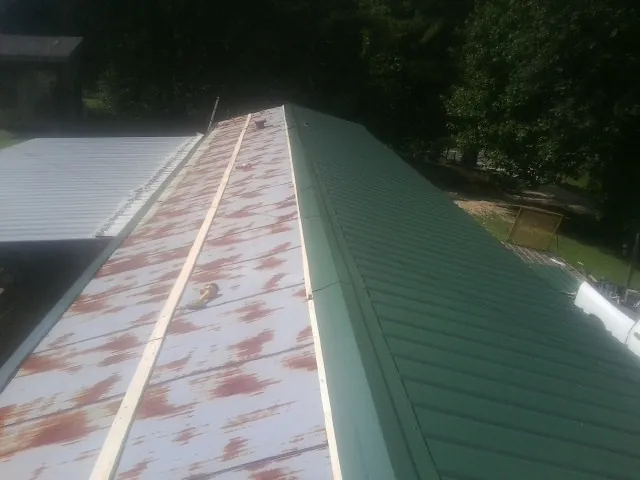 Old rusted panels beside newly installed green metal roofing — Wind Damage Roof Repair by Roofing Brothers in Olsburg