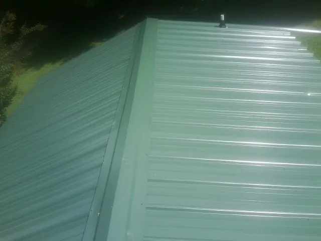 New green metal panels meeting at the ridge of a roof — Flat Roof Repair work by our crew in Olsburg