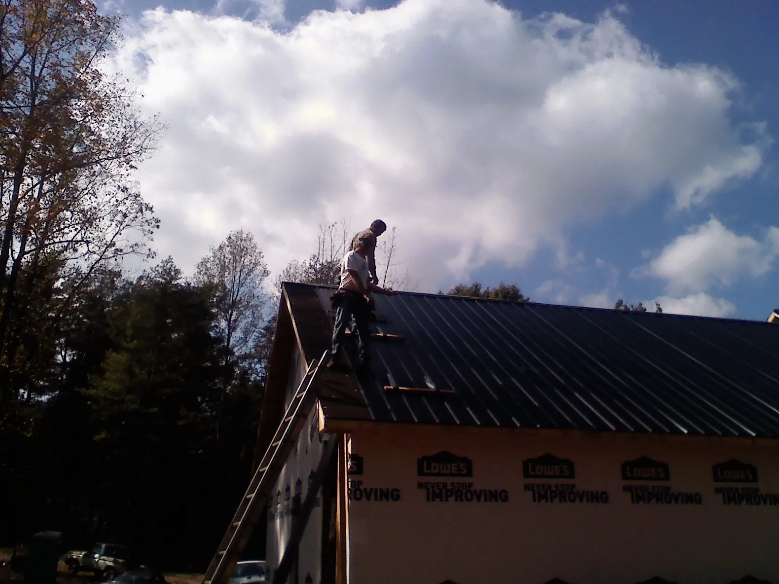 Roofer fastening dark metal panels high against a cloudy sky, from a Roof Inspection job in Olsburg