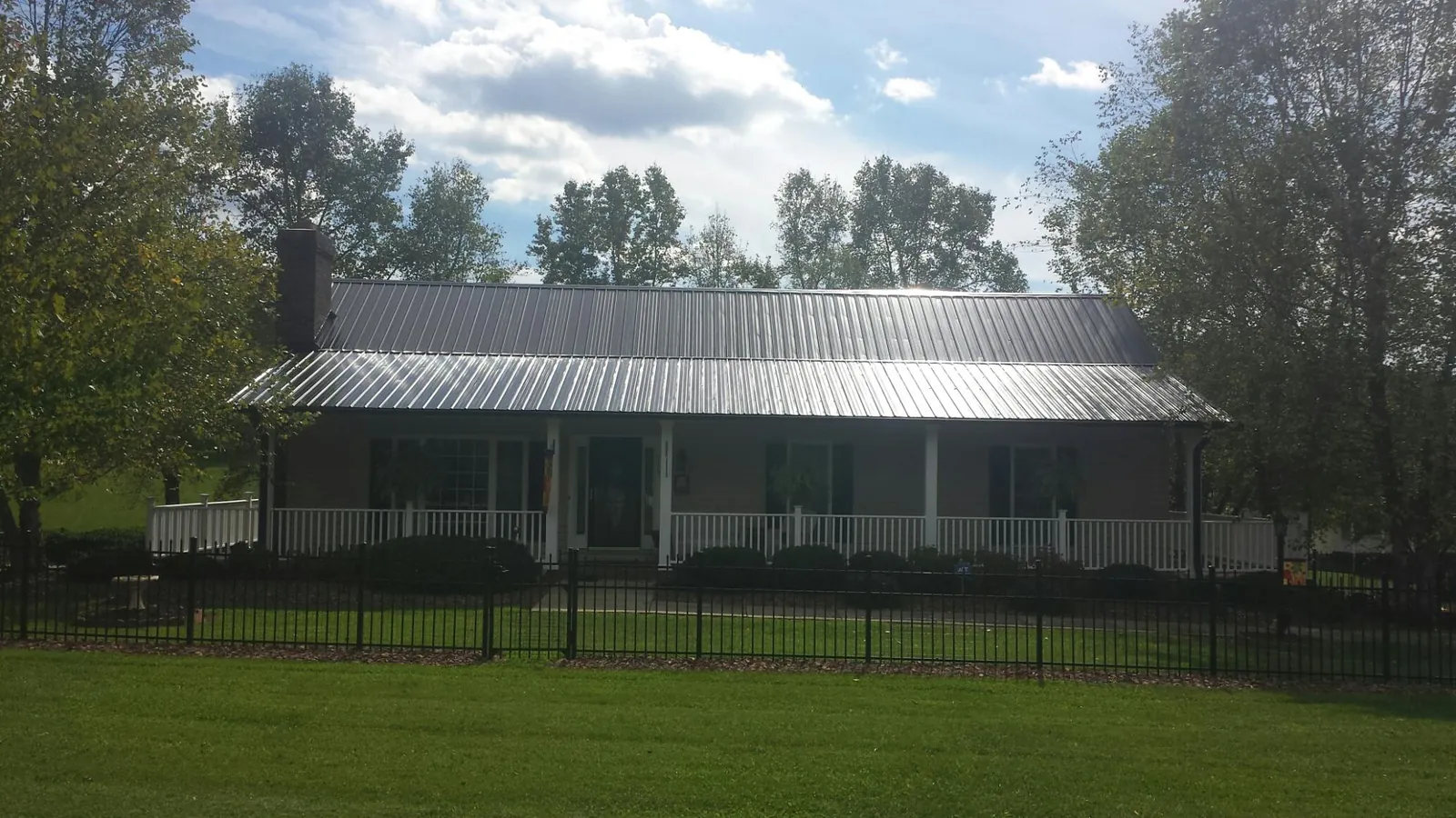 Gray metal roof on a brick ranch with a full width front porch — Gutter Guard Installation work by our crew in Olsburg