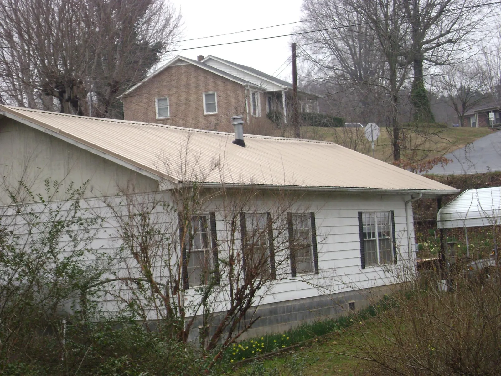 Tan metal roof on a white sided house set into a hillside — Commercial Roofing by Roofing Brothers in Olsburg