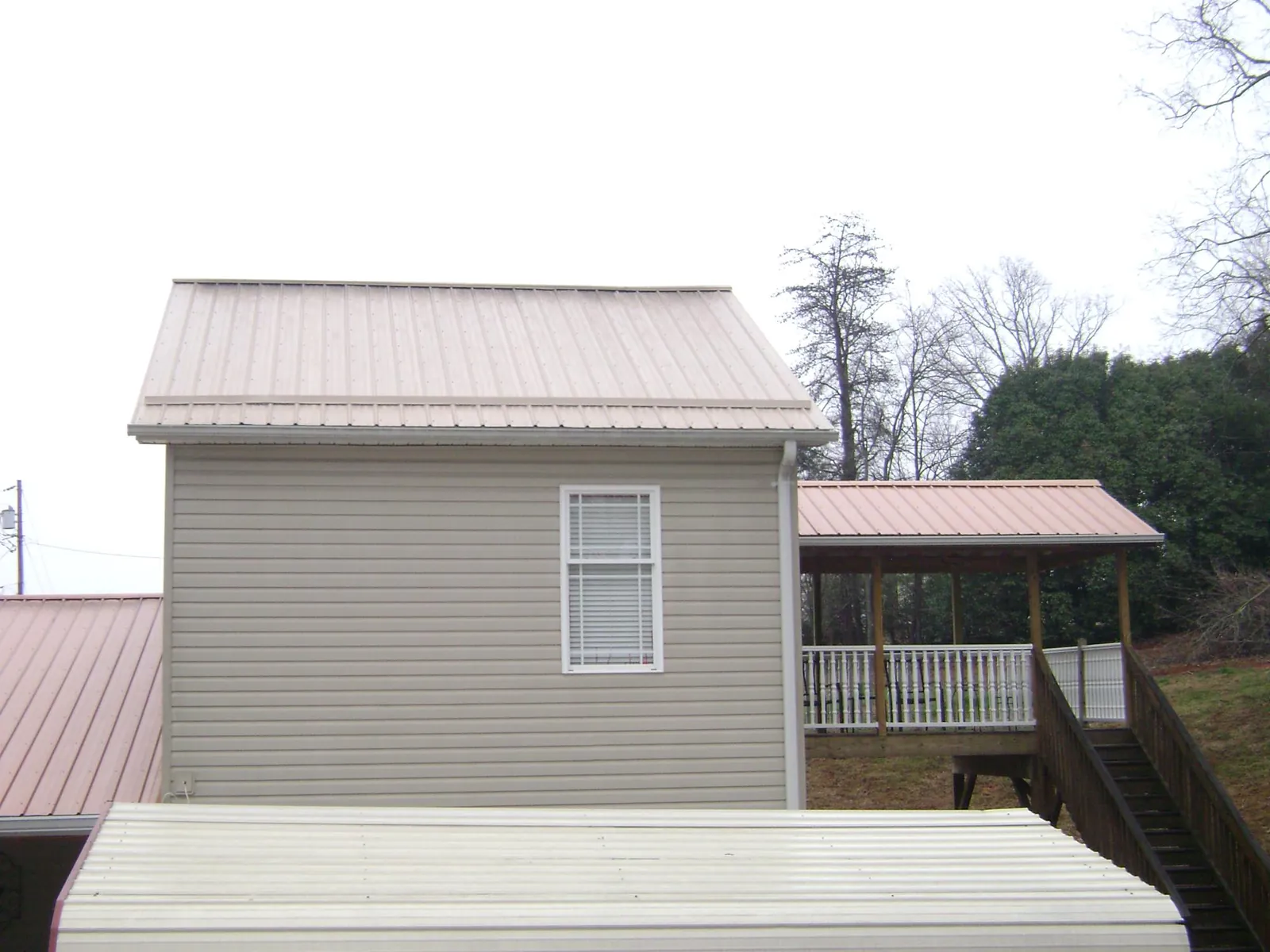 Tan metal roofs on a two story addition and attached porch, from a Roof Replacement job in Olsburg