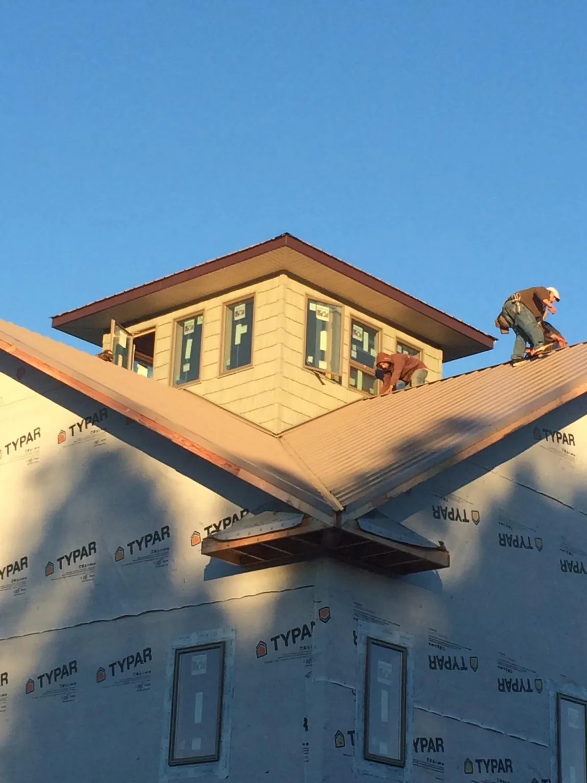 Roofers working around a rooftop cupola on a new metal roof at sunset — Roof Waterproofing in Olsburg by Roofing Brothers